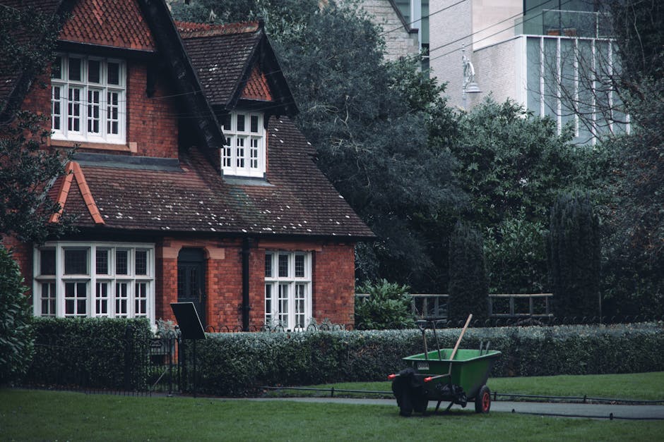 A cozy red brick house surrounded by greenery with a green wheelbarrow in the garden.